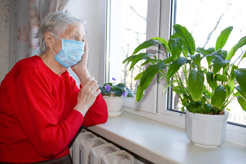 Elderly woman in disposable mask stares out of window